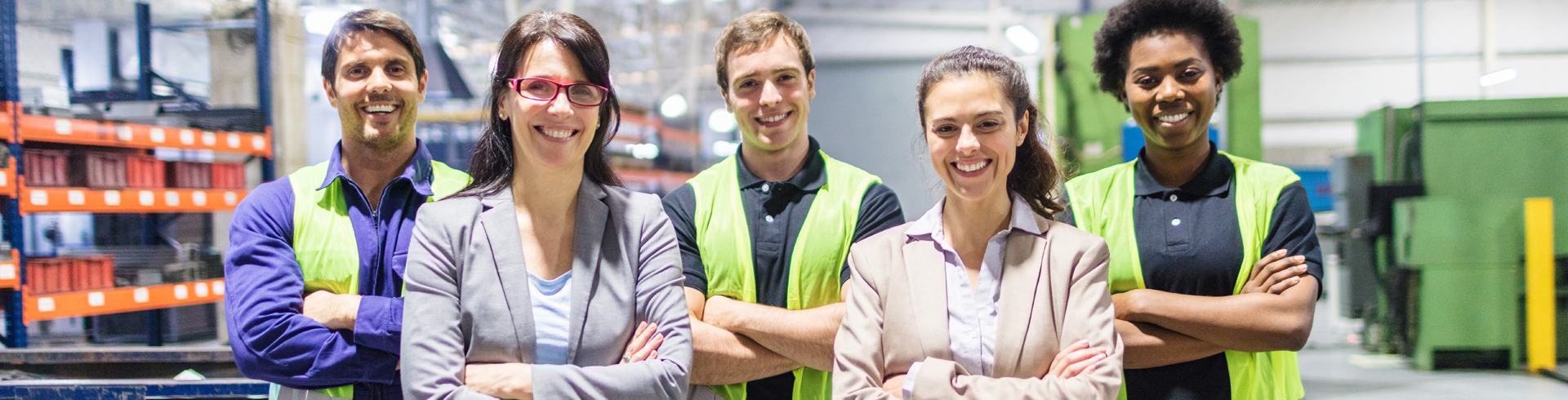 two men and three women standing in a factory, wearing yellow safety vests and crossing their arms