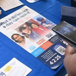 A woman uses her phone to scan a QR code on a ChattState Give Day poster.