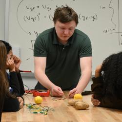Students look on as an instructor attaches an LED light to a potato and lemon to demonstrate nuclear power.