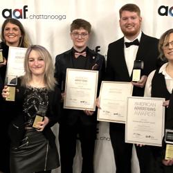 Seven ADDY Award winners in formal attire stand side-by-side holding their awards. Left to right: Sam Hammond, Tess Little, Kaitlyn Whalen, Jaden Bane, Christopher Phillips, Allison Ferguson, and Freddy Pantaleon