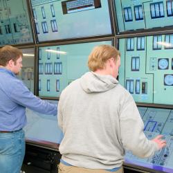 Two male students interract with an educational digital nuclear control room display.