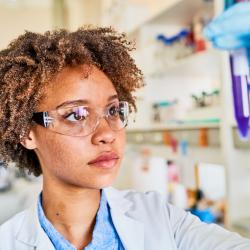 A Medical Laboratory Technician in a white lab coat looks at a medical sample in a plastic tube.