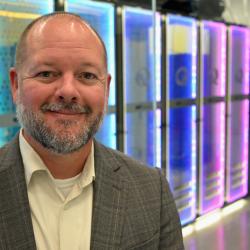 A man stands in front of colorful electronic panels.