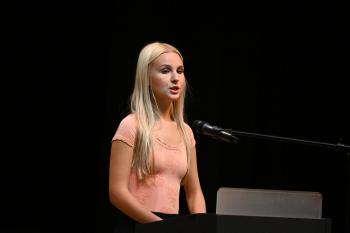 Briley wear A blonde woman in a pink shirt speaks into a microphone.