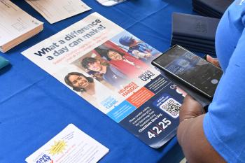 A woman uses her phone to scan a QR code on a ChattState Give Day poster.