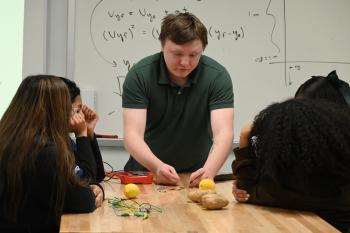 Students look on as an instructor attaches an LED light to a potato and lemon to demonstrate nuclear power.