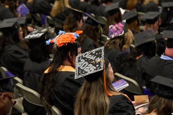 A woman sititng in a crowd of graduates wears a decorated mortaboard that reads "Class of 2025"