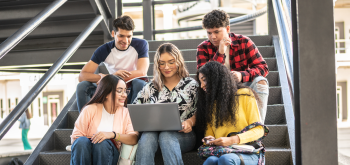 Stock photo of five college-aged students sitting on stairs looking at a laptop. Stock photo of five college-aged students sitting on stairs looking at a laptop.