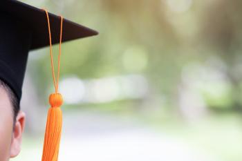 Partial view of an ambiguous student's face wearing a black mortarboard and orange tassle. Out of focus trees are visible in the background.