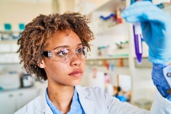 A Medical Laboratory Technician in a white lab coat looks at a medical sample in a plastic tube.