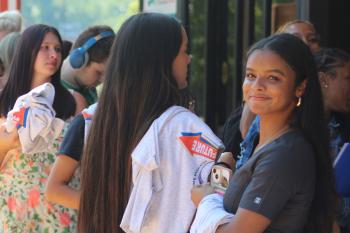 Op-Ed Image A brunette woman looks into the camera with several people standing behind her holding tee shirts.