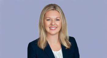 Tiffanie Robinson, a blonde woman in a black coat, smiles in front of a light blue background. Tiffanie Robinson, a blonde woman in a black coat, smiles in front of a light blue background.