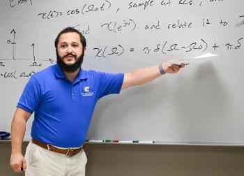 Eight years after arriving at UTC, Dr. Joshua H. Tyler now holds three degrees from the University and has transitioned into a postdoctoral researcher and faculty role. A man in a blue polo shirt points to a white board.