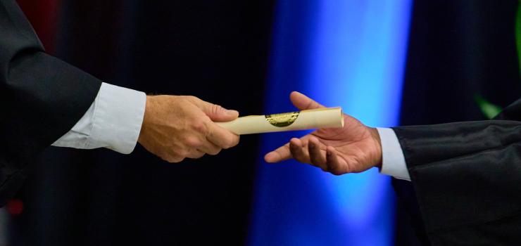 A close up of one person handing a diploma to another person.