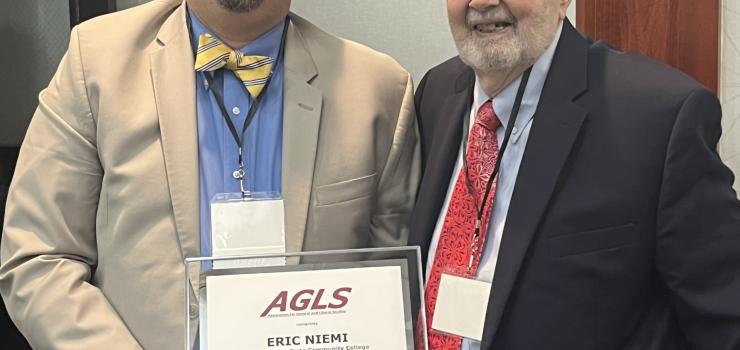 Two men pose side by side holding an award